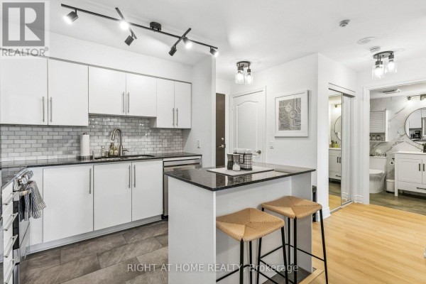 Modern kitchen with white cabinets, granite island, stainless steel appliances, and open doorway to bathroom. - 805 - 1103 Leslie Street, Toronto