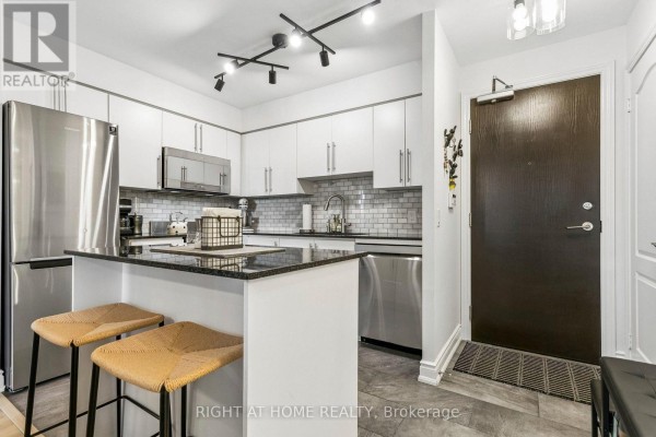 Kitchen with white cabinets, granite island, stainless steel appliances, and entrance door to the right. - 805 - 1103 Leslie Street, Toronto
