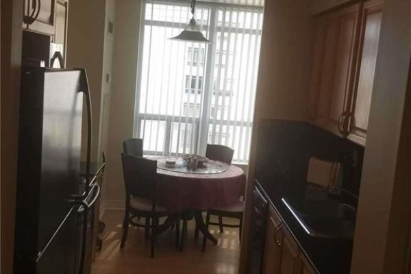 Kitchen with stainless steel refrigerator, wooden cabinets, granite countertops, and dining table by window. - 805 - 310 Burnhamthorpe Road W, Mississauga