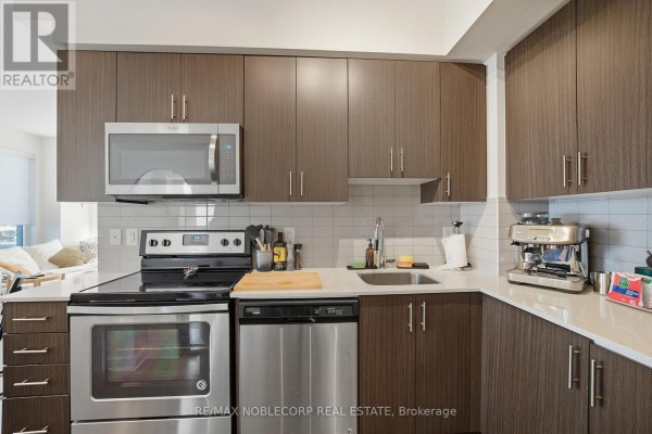 Kitchen with dark wood cabinets, stainless steel appliances, and white backsplash. - 805 - 3600 Highway 7 Road, Vaughan