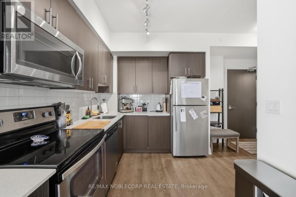 Apartment kitchen with dark wood cabinetry, stainless steel appliances, and wooden flooring. - 805 - 3600 Highway 7 Road, Vaughan