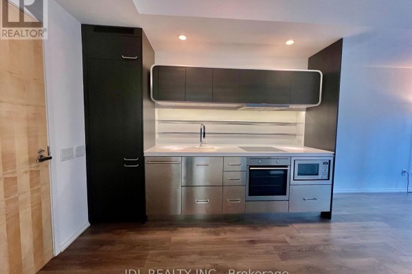 Modern galley kitchen with stainless steel appliances, dark wood cabinetry, and a light wood door. - 805 - 45 Charles Street, Toronto