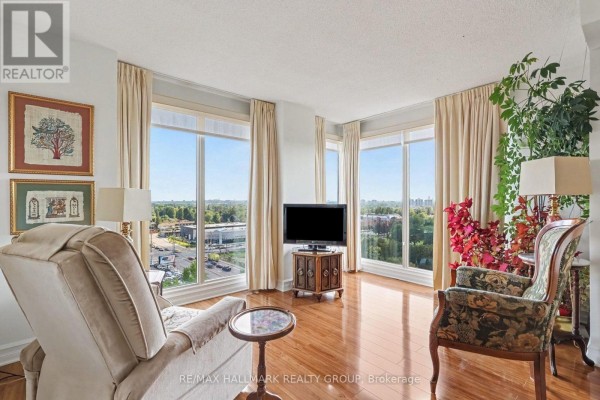 Living room with large windows, light-colored curtains, hardwood floors, chairs, and a television. - 805 - 545 St Laurent Boulevard, Ottawa
