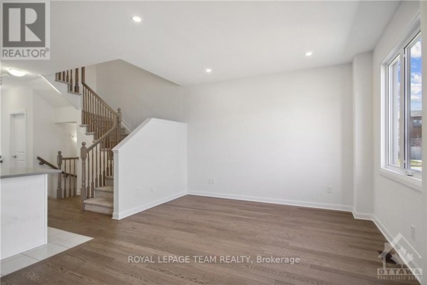 Living area with hardwood floors, white walls, a view of a wooden staircase, and a window. - 805 Everbloom Lane, Ottawa