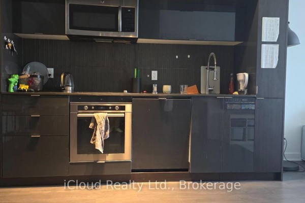Modern kitchen with dark cabinets, stainless steel appliances, and a tiled backsplash. - 806 - 28 Avondale Avenue, Toronto