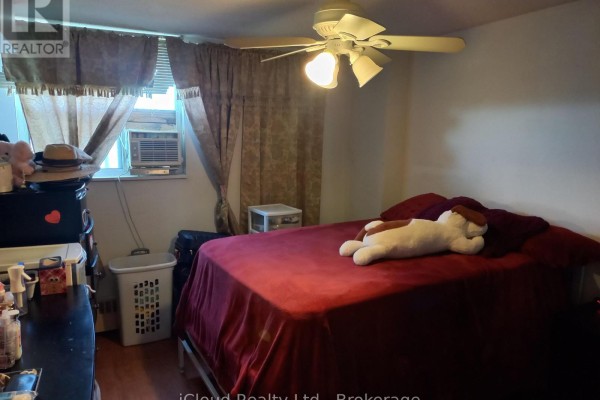 Bedroom with a red comforter, ceiling fan, and items on a dresser and in a laundry hamper. - 806 - 390 Dixon Road, Toronto