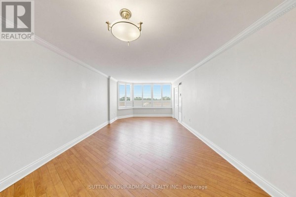 Empty room with light wood floors, white walls, and a bay window with white shutters. - 806 - 7460 Bathurst Street, Vaughan