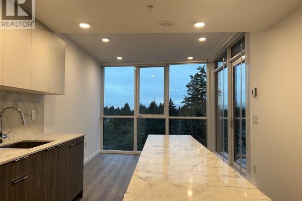 Kitchen island and cabinetry with a large window and glass door offering a view of trees. - 806 10333 133 Street, Surrey