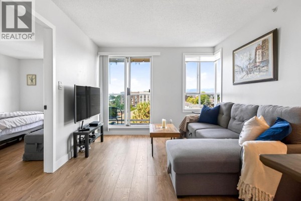 Living room with grey sectional sofa, television, and an open doorway showing a bedroom. - 806 3455 Ascot Place, Vancouver