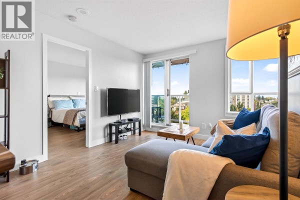Living room with grey sectional sofa and view into bedroom with blue bedding. - 806 3455 Ascot Place, Vancouver