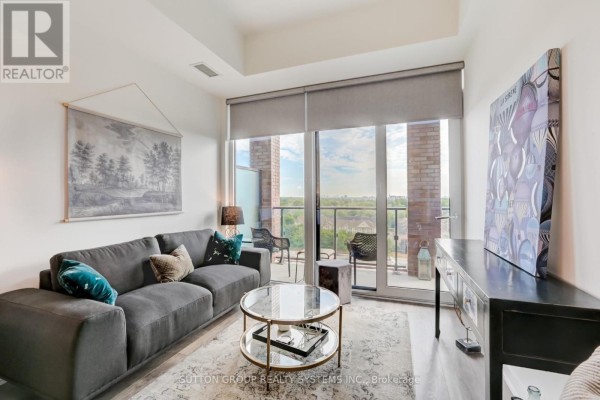 Living room with a grey sofa, balcony access, and a large abstract artwork on the wall. - 807 - 28 Ann Street, Mississauga