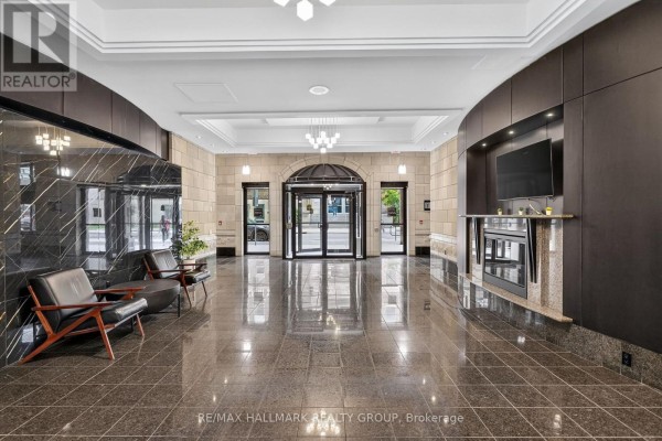 Luxury apartment building lobby with polished dark granite floors, leather chairs, and a modern fireplace. - 807 - 435 Albert Street, Ottawa