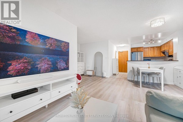 An open-concept living area with a large TV, dining table, and kitchen with wood cabinets. - 807 - 7 Lorraine Drive, Toronto