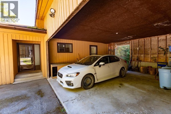 White car parked in an open, wood-paneled garage with concrete floor. - 807 Spokane Street, Rossland