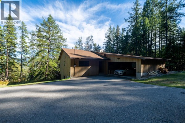 View of the house from the driveway showing the garage and surrounding trees. - 807 Spokane Street, Rossland