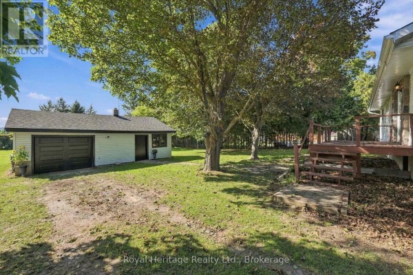 Rear view of the bungalow showing detached garage, deck, and grassy yard. - 8074 Tinkerville Road, Port Hope