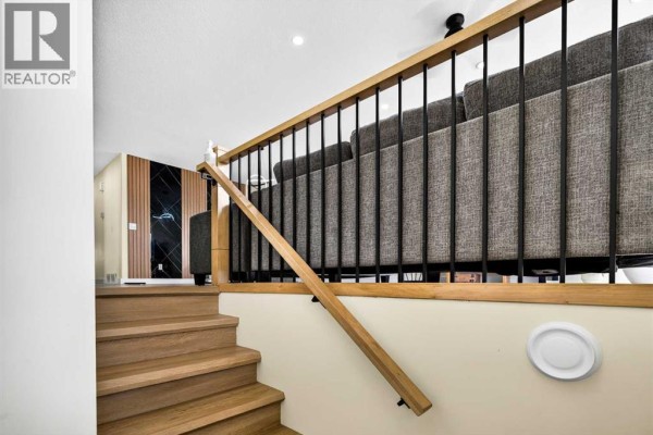 Wooden staircase with a light beige wall and a gray couch in the background. - 8079 Laguna Way Ne, Calgary