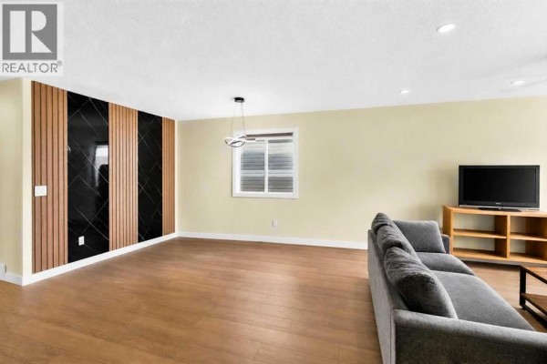 Living room with light yellow walls, wood floors, and a modern feature wall. - 8079 Laguna Way Ne, Calgary