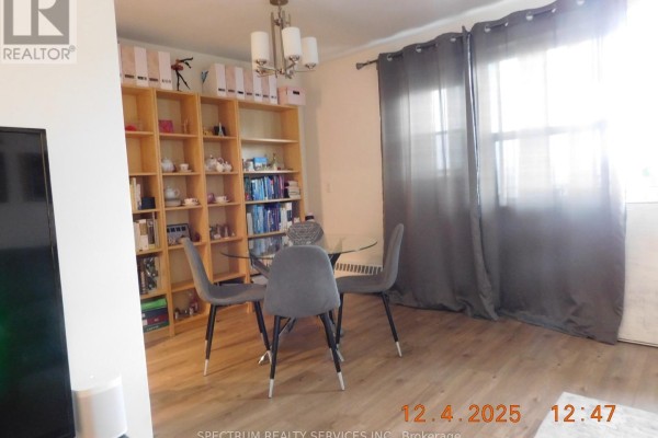 Dining area with a glass table, grey chairs, and a large wooden bookshelf. - 808 - 3320 Fieldgate Drive, Mississauga