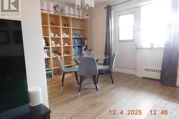 Dining area with a glass table, grey chairs, wooden bookshelf, and a doorway. - 808 - 3320 Fieldgate Drive, Mississauga