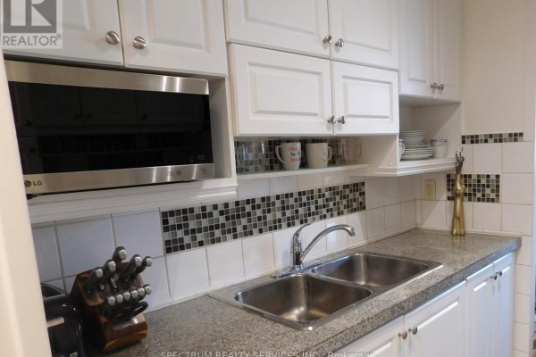 Kitchen with white cabinets, a double sink, stainless steel microwave, and mosaic backsplash. - 808 - 3320 Fieldgate Drive, Mississauga