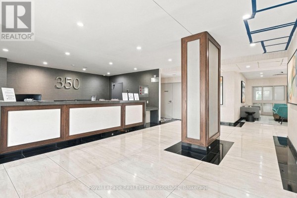 Building lobby with a reception desk, wood accents, and tiled floors. - 808 - 350 Rathburn Road W, Mississauga