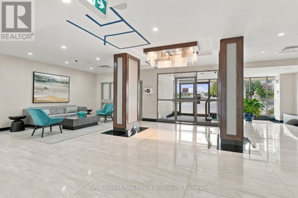 Apartment building lobby with seating area, modern art, and glass doors. - 808 - 350 Rathburn Road W, Mississauga