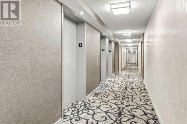 Long apartment building hallway with textured walls, elevators, and patterned carpet. - 808 - 350 Rathburn Road W, Mississauga