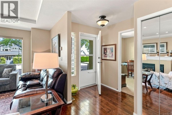 Entrance hall with hardwood floors, a glass door, a mirrored closet, and a view into a living room. - 808 Stanhope Rd, Parksville