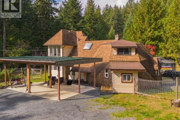 Side view of the beige house with a covered carport and adjacent wooden structures. - 8089 Daisy Road, Powell River