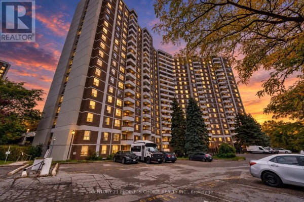 The apartment building exterior at dusk, with lights on inside and cars in the parking lot. - 809 - 10 Edgecliffe Golfway, Toronto