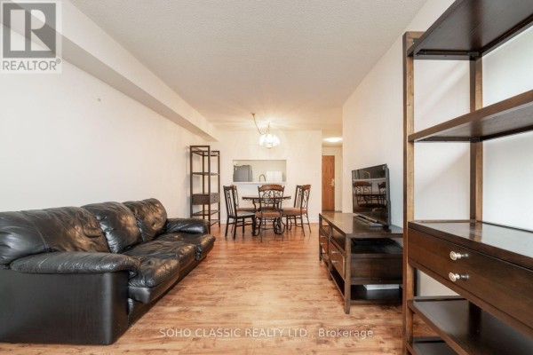 Apartment living room with black leather sofa, dining area, and wood flooring. - 809 - 1700 Eglinton Avenue E, Toronto