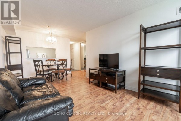 Apartment living and dining area with black sofa, TV, dining table, and shelving. - 809 - 1700 Eglinton Avenue E, Toronto