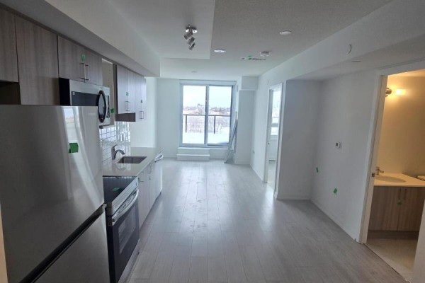 Open concept kitchen and living area with stainless steel appliances, light wood cabinets, and a large window. - 809 - 556 Marlee Avenue, Toronto
