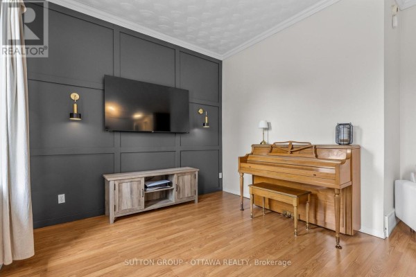 Living room focal wall with mounted TV, wood entertainment console, and upright piano. - 8097 Laurie Lane, Ottawa