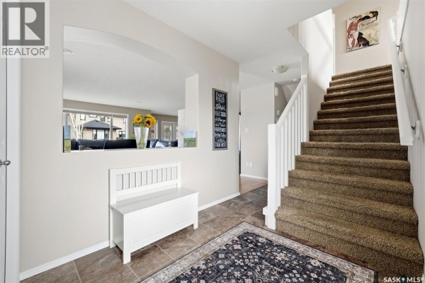 Entryway with beige walls, a white bench, a dark patterned rug, and carpeted stairs leading up. - 8097 Wascana Gardens Crescent, Regina