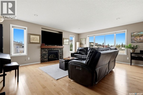 Living room with hardwood floors, a stone fireplace, a large television, and black leather sofas. - 8097 Wascana Gardens Crescent, Regina
