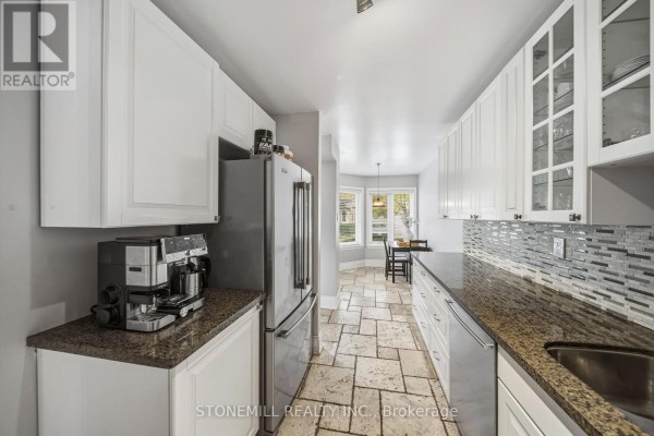 Narrow kitchen featuring white cabinets, granite counters, stainless steel fridge, and a dining nook with bay windows. - 81 - 2155 South Millway, Mississauga