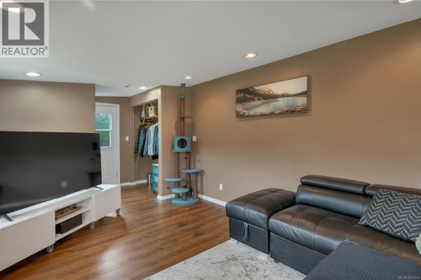 View of living room from opposite end, showing couch, TV, door, and cat tree. - 81 5250 Beaver Harbour Rd, Port Hardy