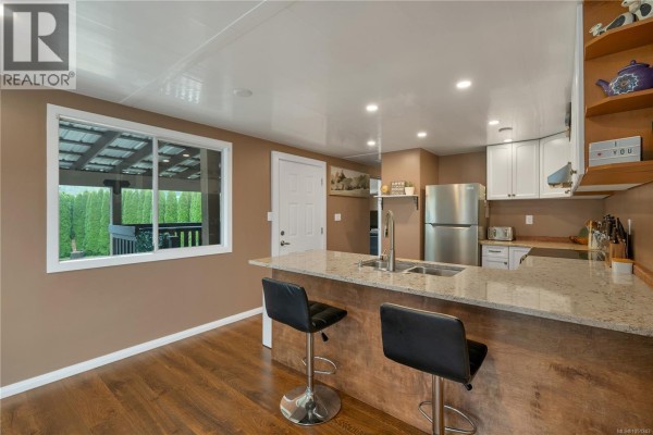 Kitchen with island, bar stools, stainless steel appliances, and white cabinets. Window overlooks deck. - 81 5250 Beaver Harbour Rd, Port Hardy