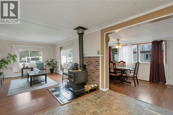 Living room with wood stove on brick hearth, wood floors, and view of dining area. - 81 951 Homewood Rd, Campbell River