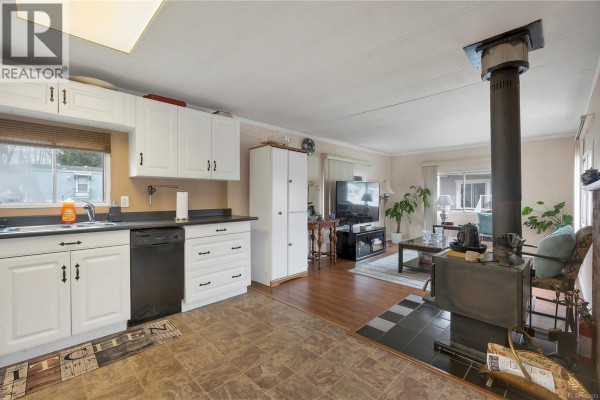 Open concept kitchen and living area with wood stove, television, and dining table. - 81 951 Homewood Rd, Campbell River