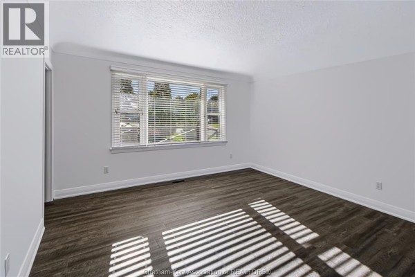 Interior view of a bedroom with white walls, dark wood-look vinyl flooring, and horizontal blinds on the window. - 81 Devon Road, Chatham