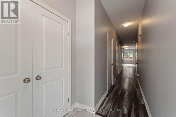 Hallway with light grey walls, white doors, and dark wood laminate flooring. - 81 Grove Street, Welland