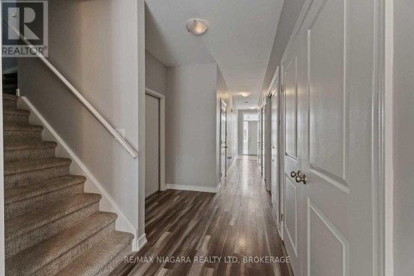 Hallway with a carpeted staircase on the left and white doors on the right. - 81 Grove Street, Welland
