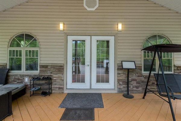 Front door view of a beige house with stone skirting, arched windows, and outdoor seating on the porch. - 81 Reisswood Drive, Traverse Bay