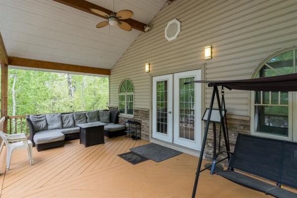 Covered porch with sectional seating, a swing, ceiling fan, and double doors, overlooking a wooded area. - 81 Reisswood Drive, Traverse Bay