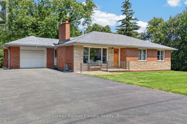 Close-up front exterior of a brick and stone bungalow with a paved driveway and green lawn. - 81 Tremaine Road, Milton