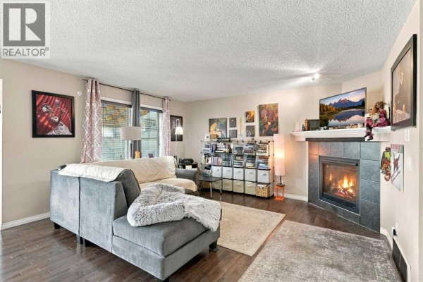 Living room with a grey sectional sofa, gas fireplace with black tile surround, and hardwood floors. - 81 Walden Rise Se, Calgary