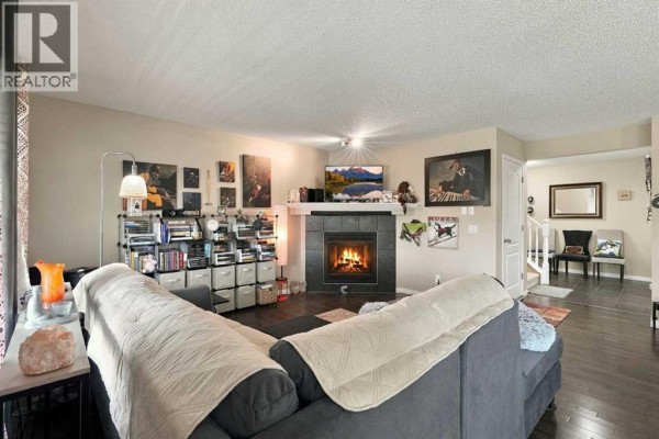 Living room with a corner gas fireplace, dark hardwood floors, and a doorway leading to another room. - 81 Walden Rise Se, Calgary